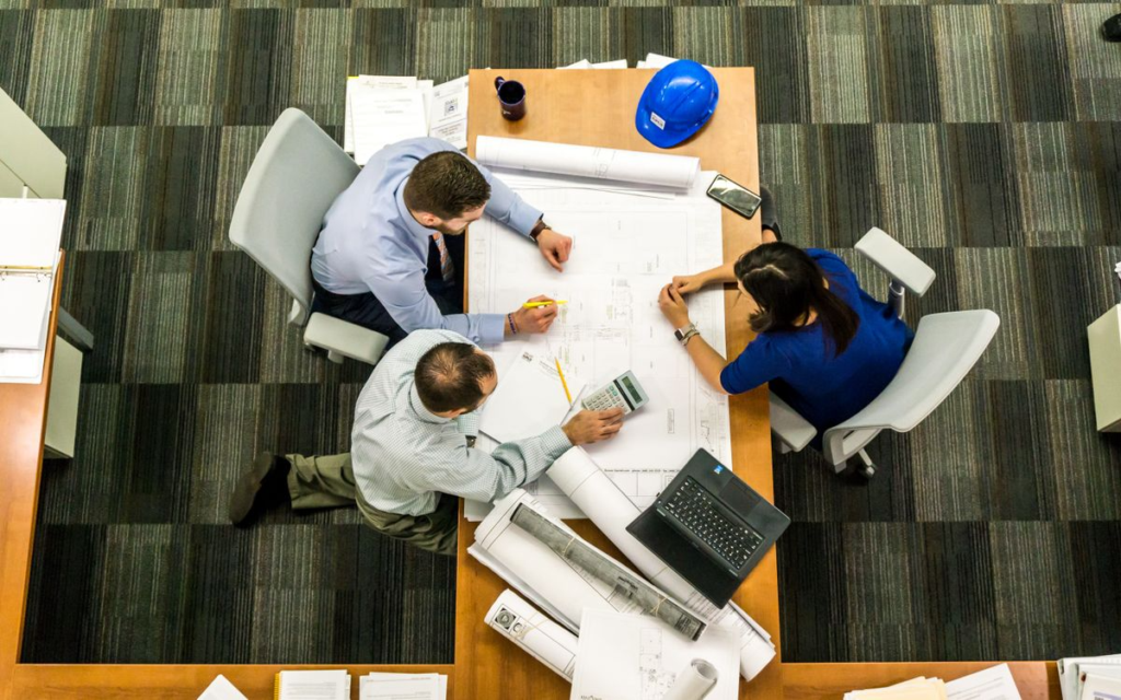 Professionals sit at a table to discuss building plans and financial logistics for a project.