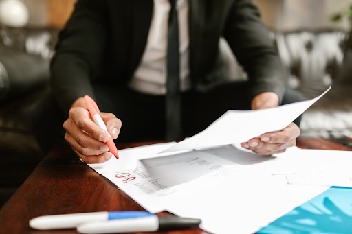 A business owner reviewing job paperwork, contracts and invoices at a desk, circling numbers in red marker.