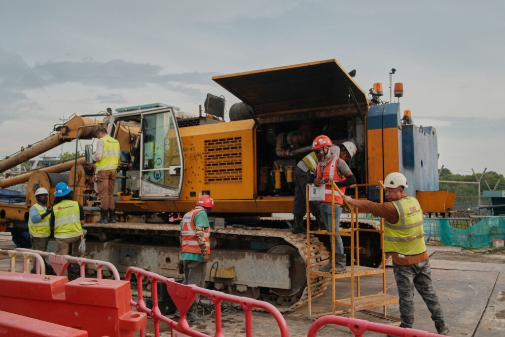 A crew of construction workers in hard hats and high-visibility vests works around a large yellow crane at an active job site.