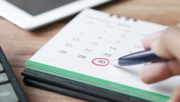 A person at a desk circling a calendar date with a red pen.