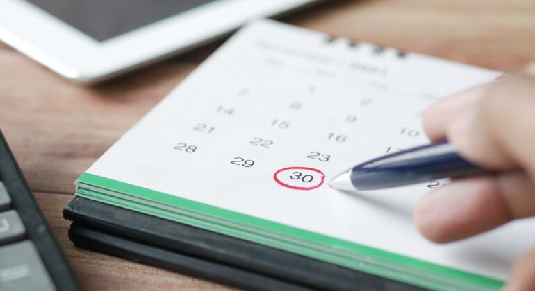 A person at a desk circling a calendar date with a red pen.